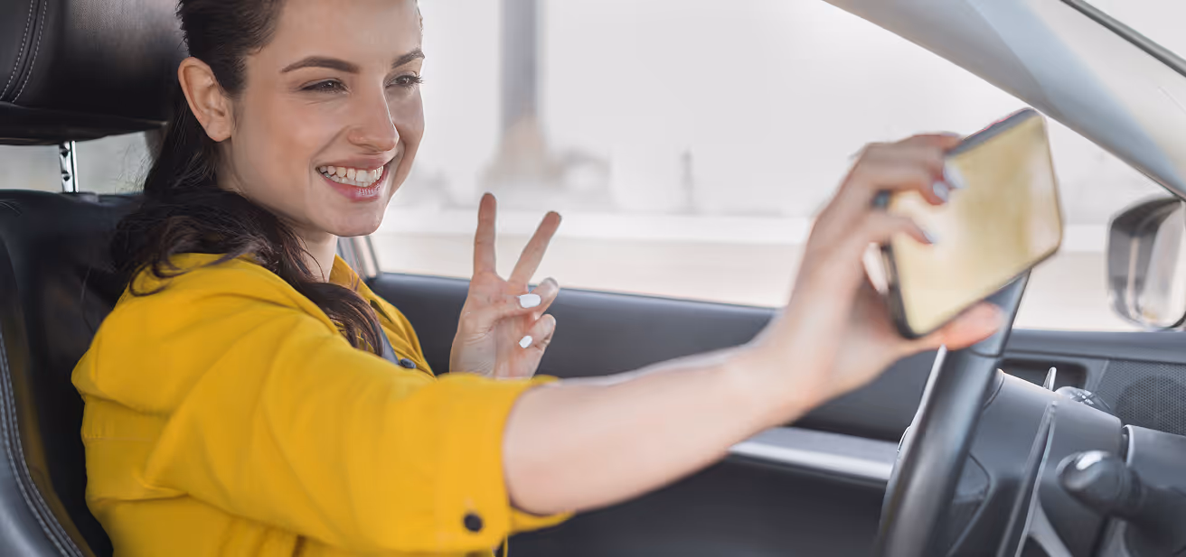Fahrschülerin macht im Auto ein Selfie mit Victory-Zeichen