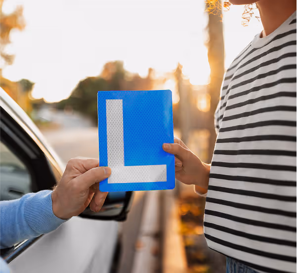 Fahrlehrer übergibt einer Fahrschülerin das L-Schild